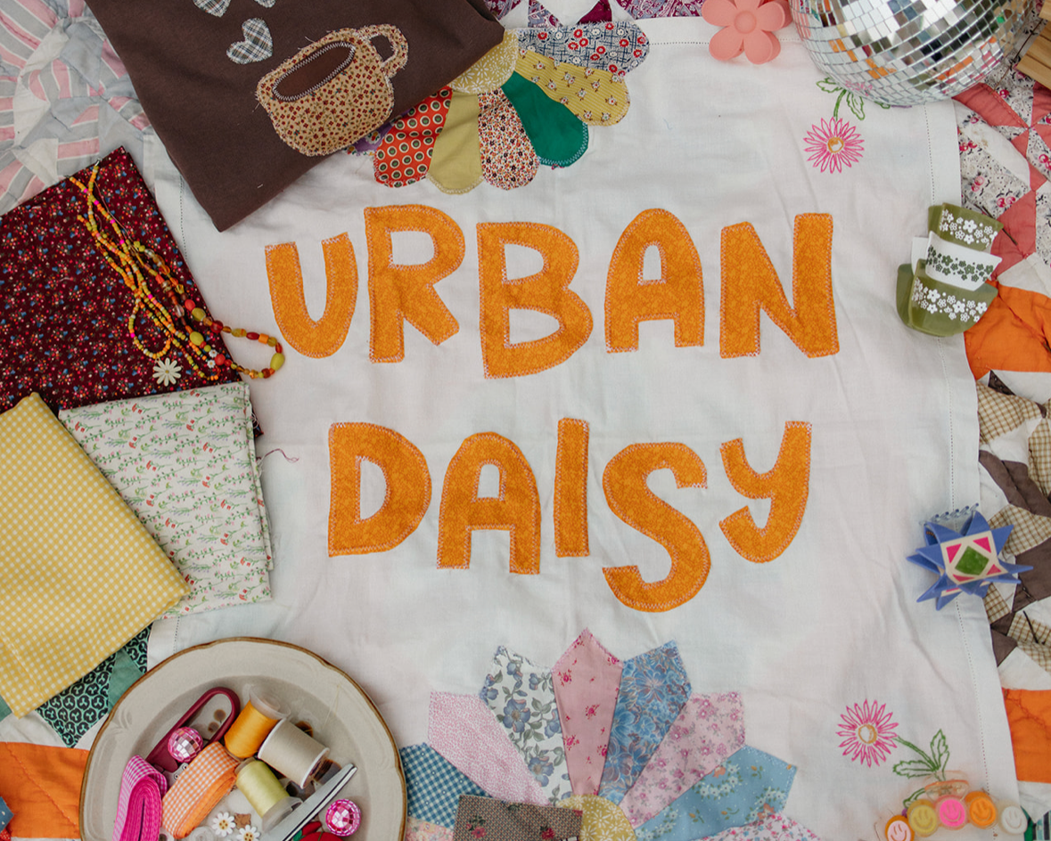 Colorful quilt with 'Urban Daisy' text and various items on a phone screen.
